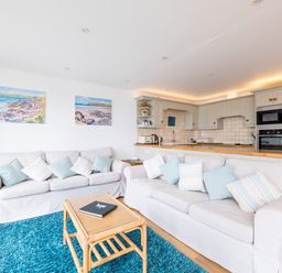 A living room with two white sofas and a wooden coffee table on a blue rug next to a kitchen with beige cabinets at Slipway 21 in Rock