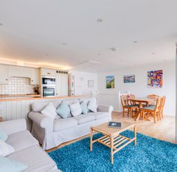 An open living room with two sofas and a blue rug next to a kitchen with white cabinets and wooden dining table with chairs at Slipway 21 Rock