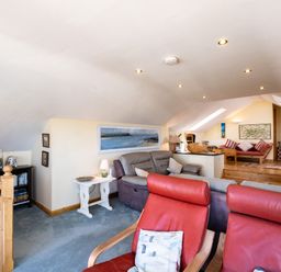 A living room with sofas red armchairs a wooden bookcase and a television at Little Belz in Polzeath