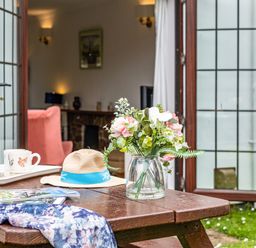 A garden table with a vase of flowers a hat a scarf and a tray with a teapot and mugs outside open doors to a living room at Hazelhurst in Rock