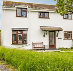 A white two-story house with brown windows a bench outside and green lawn at Hazelhurst in Rock