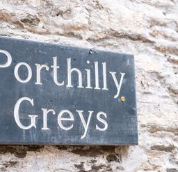 A stone wall with a black rectangular sign reading Porthilly Greys