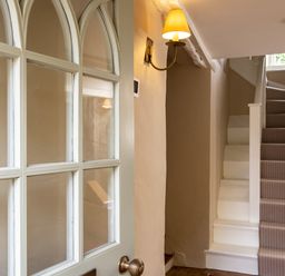 A staircase with a striped carpet and a wall lamp next to a door with glass panels at Porthilly Greys in Rock