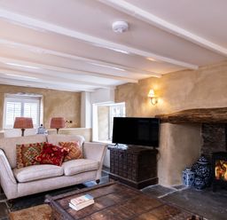 A sitting room with a beige sofa with patterned cushions a wooden coffee table a television on a wooden cabinet and a wood burning stove at Porthilly Greys in Rock