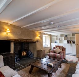 A living room with a wood-burning stove a wooden coffee table armchairs and built-in shelves at Porthilly Greys Rock