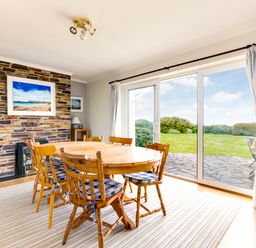 A dining area with a wooden table and chairs near sliding glass doors overlooking a garden at Trebartha Daymer Bay