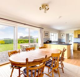 A kitchen and dining area with wooden table and chairs near sliding glass doors opening to a garden at Trebartha in Daymer Bay