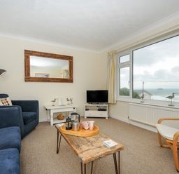 A living room with blue sofas a wooden coffee table a television and large window overlooking the sea at Trevega Polzeath