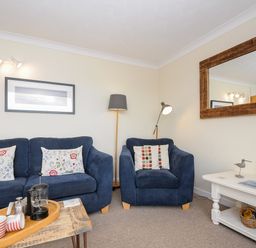 A living room with blue sofa and armchair a wooden coffee table and white side table with decorative items at Trevega Polzeath