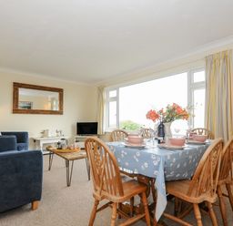 A dining table with six wooden chairs set with dishes and flowers next to a sitting area with blue sofas and a coffee table at Trevega Polzeath