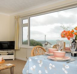 A dining area with a table set with plates bowls wine glasses and flowers next to a window with a sea view at Trevega in Polzeath