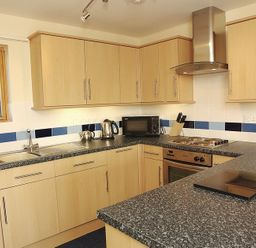 A kitchen with wooden cabinets a stove microwave kettle and sink at Polzeath Court 4 in Polzeath