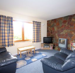 A living room with two black leather sofas a wooden coffee table a TV on a stand a stone wall and checked curtains at Polzeath Court 4 in Polzeath