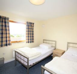 A bedroom with two single metal frame beds a wooden nightstand and a window with checkered curtains at Polzeath Court 4 Polzeath