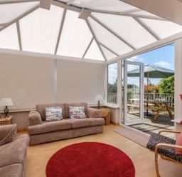 A conservatory with sofas and armchair around a round red rug and glass door leading to a patio at Cogenhoe in Rock