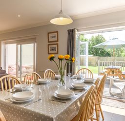 A dining room with a table set for eight people and sunflowers in a vase by open doors leading to a garden at Cogenhoe in Rock
