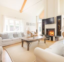 A living room with white sofas wooden coffee table fireplace and a television at Ragleighs in Daymer Bay