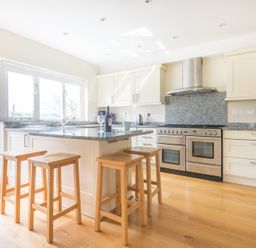 A kitchen with a central island and wooden stools and stainless steel appliances at Ragleighs in Daymer Bay
