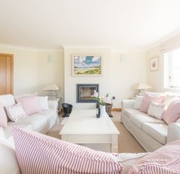 A living room with two white sofas and a white coffee table with flowers in a vase at Ragleighs in Daymer Bay