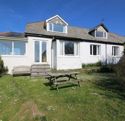 A white house with multiple windows and a wooden picnic table on a grassy lawn at Gullsway Kittiwake in Polzeath
