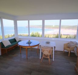 A room with multiple windows overlooking the sea with tables chairs and a wooden sideboard at Gullsway Kittiwake in Polzeath