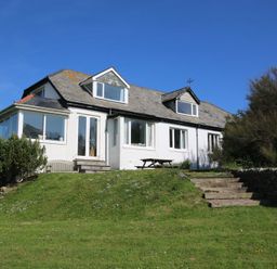 A white house with a slate roof surrounded by grass and bushes at Gullsway Sandpiper Polzeath