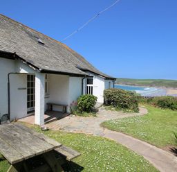 An exterior view of a white house with a slate roof a picnic table on grass and a beach in the background at Gullsway Sandpiper Polzeath