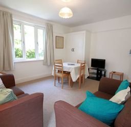 A living room with brown sofas and teal cushions a dining table with chairs and a small television in the corner at Gullsway Sandpiper Polzeath