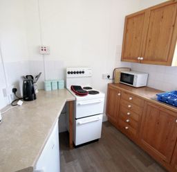 A kitchen with wooden cabinets a white stove a microwave a kettle toaster and a dish drying rack at Gullsway Sandpiper Polzeath