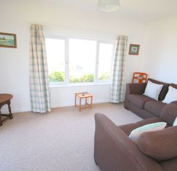 A living room with brown sofas white cushions a small wooden table lamp and plaid curtains at Gullsway September Tide in Polzeath
