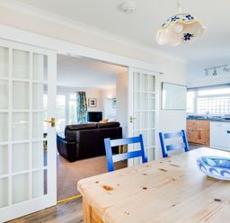 A kitchen and dining area with wooden furniture blue chairs and a living room with a brown sofa at Little Sailing in Rock