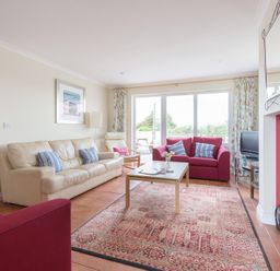 A living room with a cream sofa two red armchairs a coffee table and a television at Kirra in Polzeath