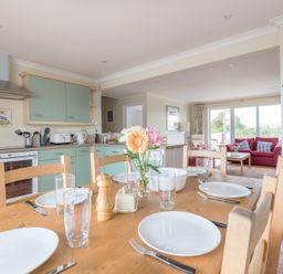 A dining table with plates glasses and flowers in a kitchen and living room at Kirra in Polzeath