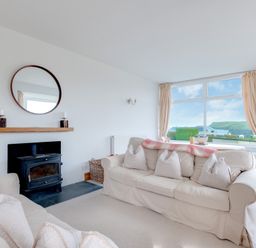 A living room with two sofas a wood stove and a large window with curtains at Pentire View Polzeath