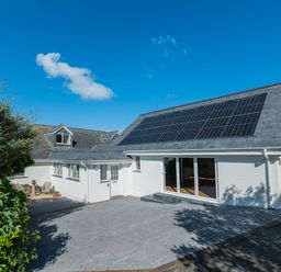 A white house with solar panels on the roof and a paved driveway at Treverden in Polzeath