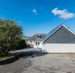 A driveway with a white house and a tree under a blue sky at Treverden Polzeath