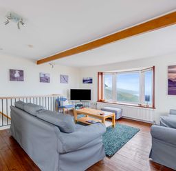 A sitting room with grey sofas a wooden coffee table a blue rug and a large window at Shilling Stones in Port Isaac