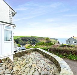 A stone patio with a low stone wall overlooking green hills and the sea at Shilling Stones in Port Isaac