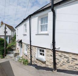 A white cottage with stone lower walls and black drainpipes beside a narrow street at Bre Cottage in Port Isaac
