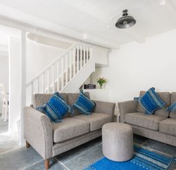 A living room with two grey sofas and blue cushions near a staircase at Bre Cottage in Port Isaac