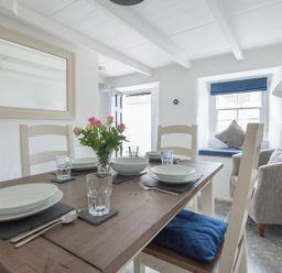 A dining area with set table with plates glasses and cutlery and a window seat with cushions at Bre Cottage in Port Isaac