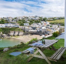 A picnic table with bottles and a magazine on the grass overlooking a harbor and village at Folly 2 in Port Isaac