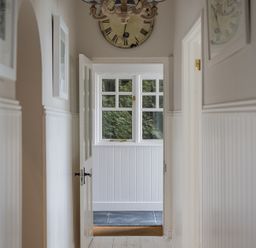 A hallway with doors and a window at the end under a wall clock at Folly 2 in Port Isaac