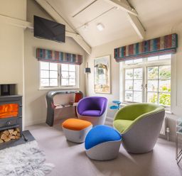 A living room with colorful chairs and a small stove at Crow's Nest in Port Isaac