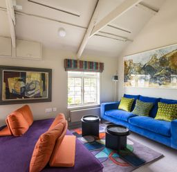 A living room with a blue sofa and orange cushions next to a purple sofa and colorful rug at Crow's Nest in Port Isaac