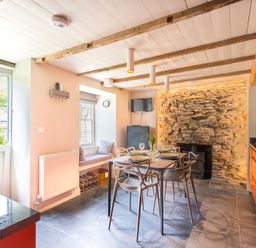 A kitchen and dining area with a stone wall fireplace and orange cabinets at Crow's Nest in Port Isaac
