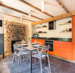 A kitchen dining area with orange cabinets stone wall and a table set with plates and glasses at Crow's Nest in Port Isaac