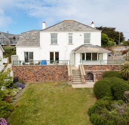 A white house with slate roof and stone terrace overlooking a garden at Worthy House in Daymer Bay