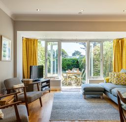 A living room with gray chairs blue sofa yellow curtains and a view to a garden at Lowenna Manor 4 in Rock