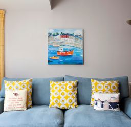 A blue sofa with yellow patterned and printed cushions against a white wall with a painting of boats above at Lowenna Manor 4 in Rock